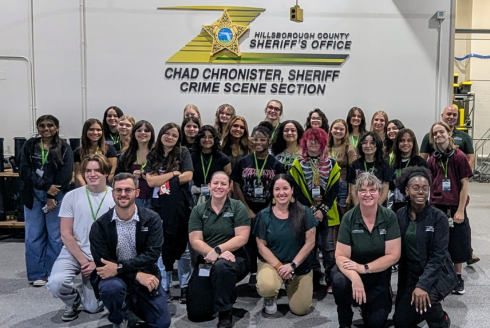 High school student camp participants taking a group photo in front of the Hillsborough County Sheriff's Office crime scene section sign
