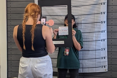 Students take photos in front of mug shot wall