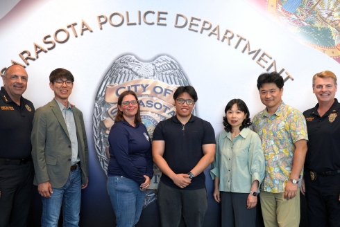 USF researchers and Sarasota Police Department personnel pose together in front of a Sarasota Police Department wall emblem