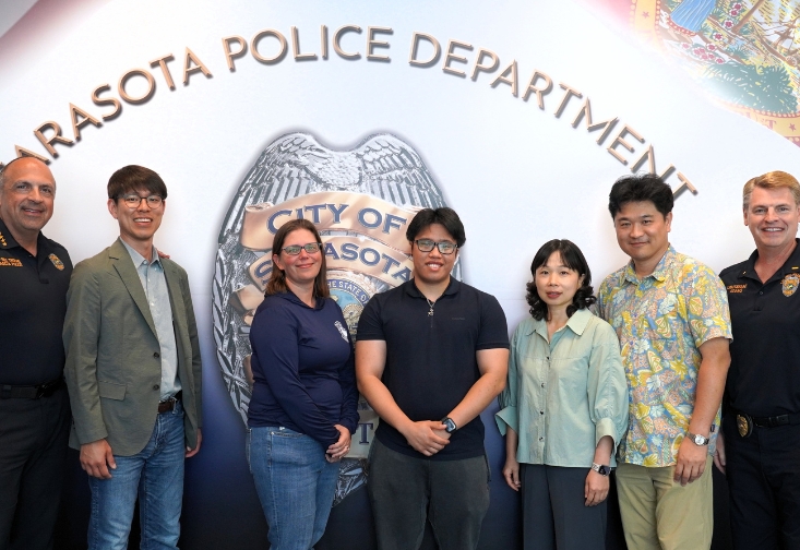 USF researchers and Sarasota Police Department personnel pose together in front of a Sarasota Police Department wall emblem