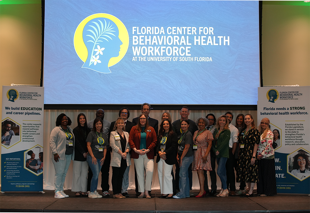Florida Center for Behavioral Health Workforce leaders take a group photo on satge with their logo in the background