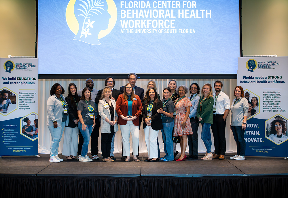 Florida Center for Behavioral Health Workforce leaders take a group photo on satge with their logo in the background