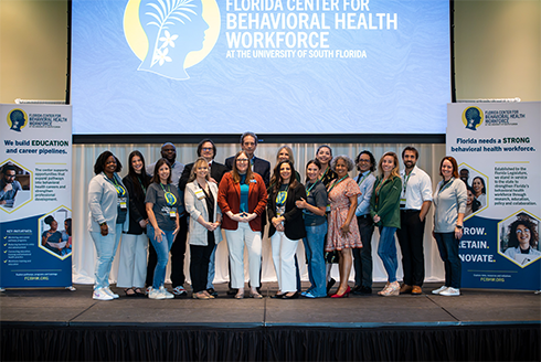 Florida Center for Behavioral Health Workforce leaders take a group photo on satge with their logo in the background