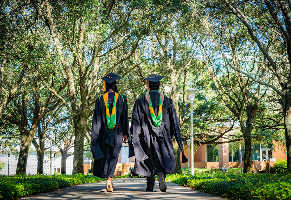 Two graduating students stand side by side, making the USF "Horns Up" hand gesture