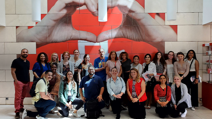 Group of people standing and kneeling in front of a mural painting of a hand making a heart.