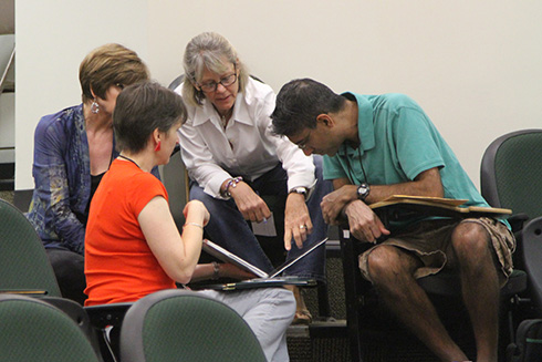 Four USF faculty working on a learning activity and looking into a book