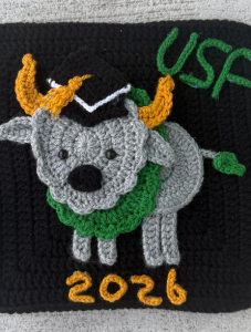 A fully knitted grad cap with a knitted Rocky the Bull and "USF 2026" knitted out in green and gold yarn. 