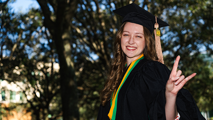 A USF grad, wearing regalia, smiles for the camera, throwing up the "Horns Up" Bulls sign.