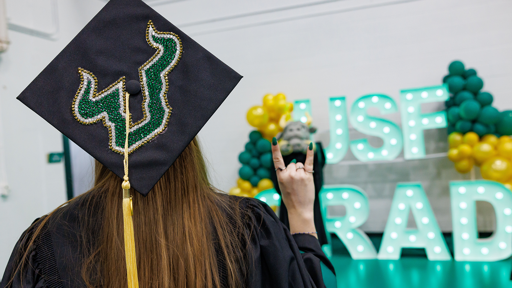 USF graduate wearing regalia facing a sign reading "USF Grad"