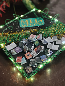 Grad cap with "MLIS Archives" and tiny paper novels