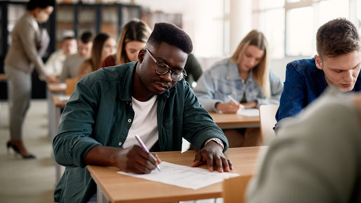 man sits in classroom writing on paper