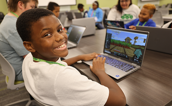 a young kid smiles at the camera while playing minecraft during summer camp at usf