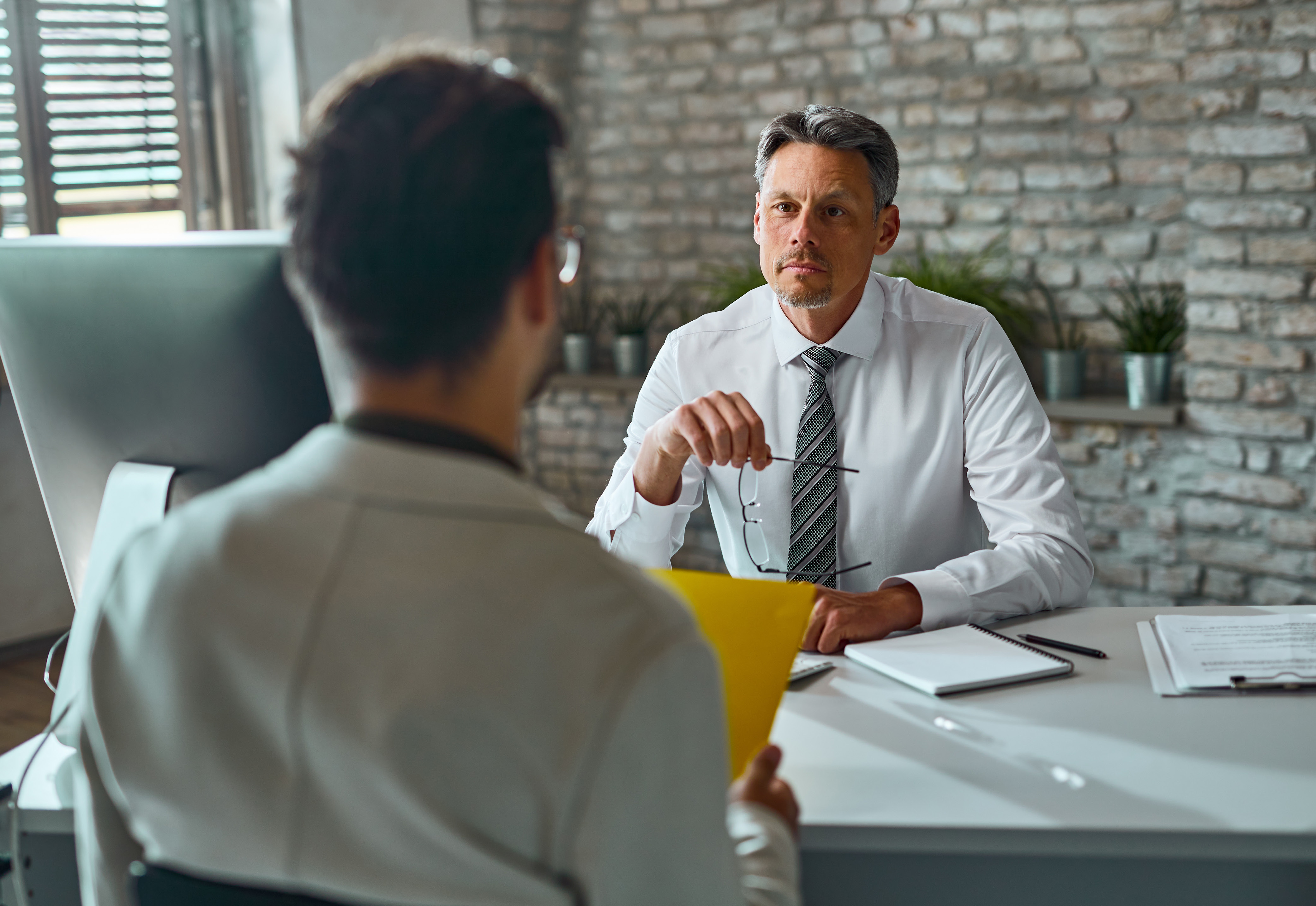 man sits across desk from another man in discussion