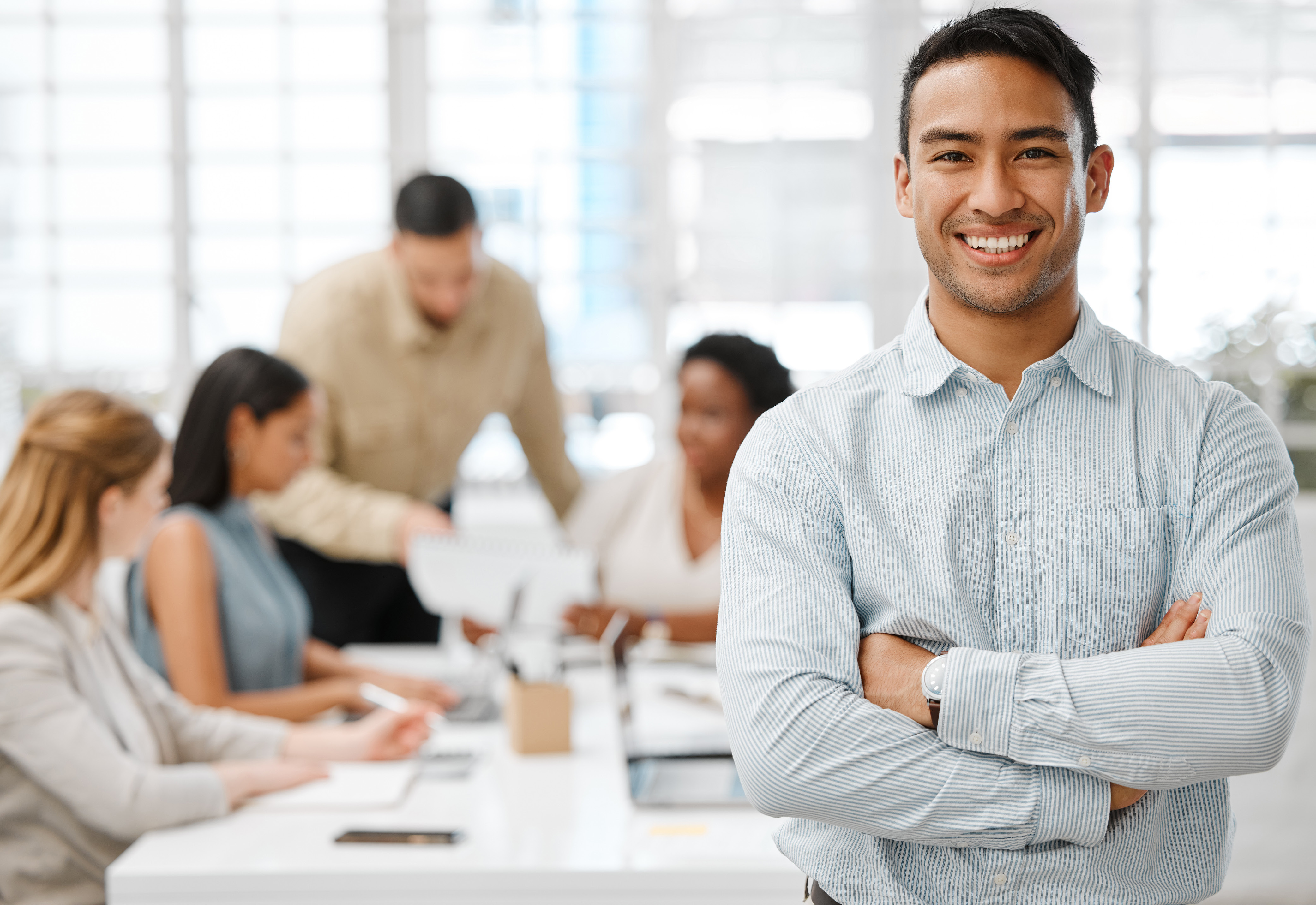 A man smiling with his arms crossed with a group of people working behind him