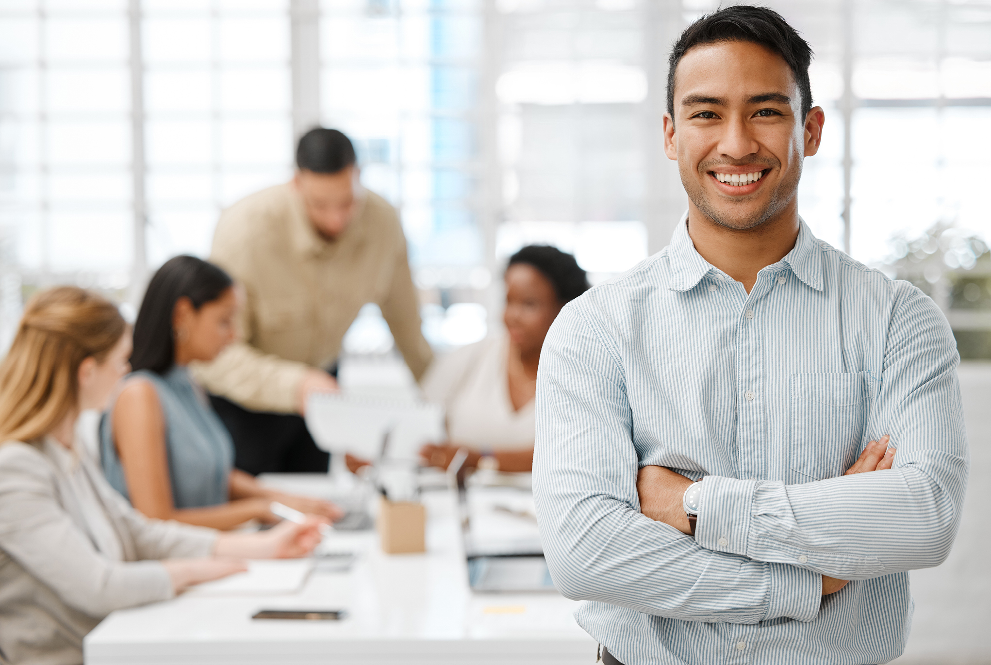 A man smiling with his arms crossed with a group of people working behind him