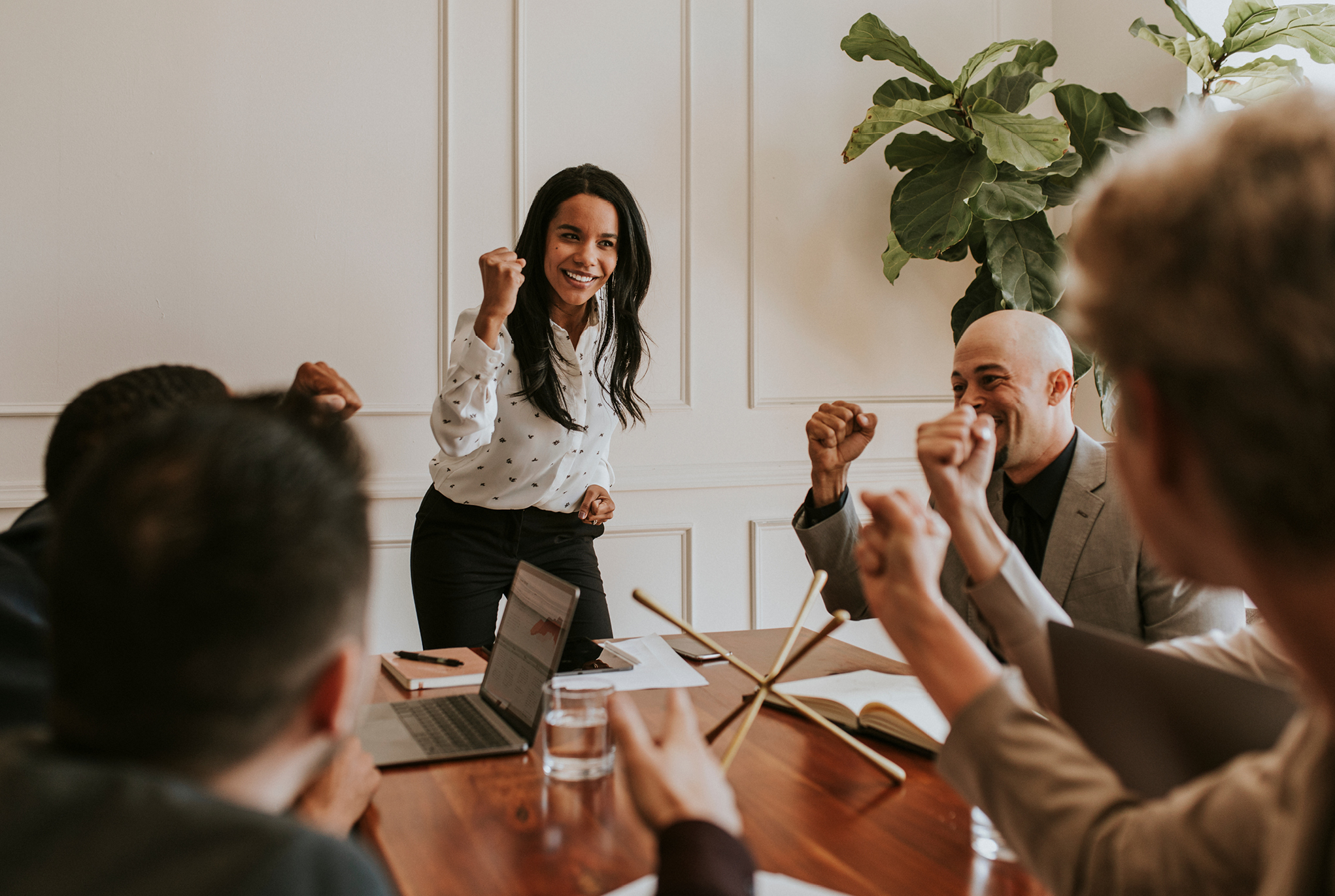 A group of people sitting around a table smiling with their fists raised in the air