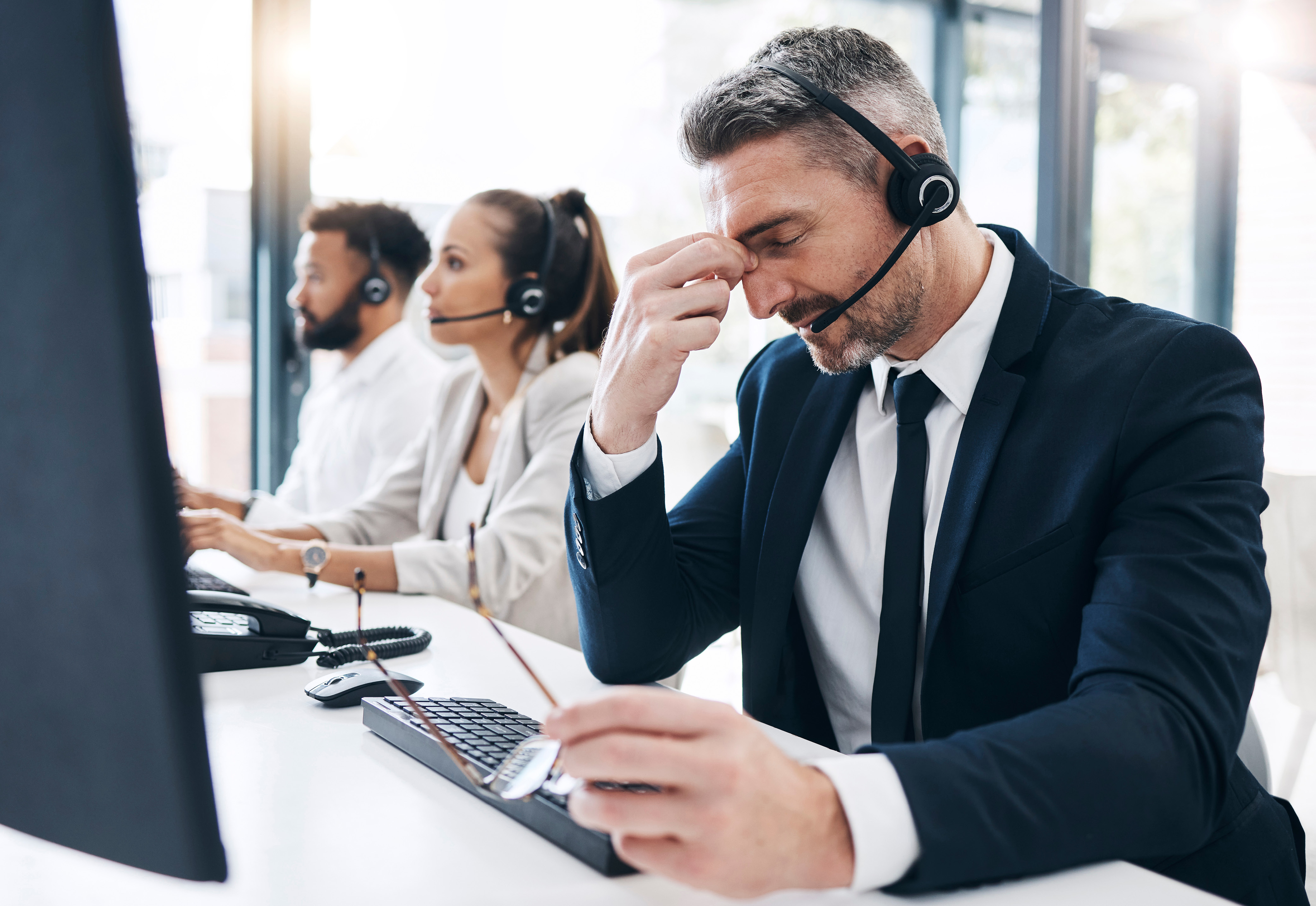 A group of three people sitting at a desk wearing headsets, with one man touching his face