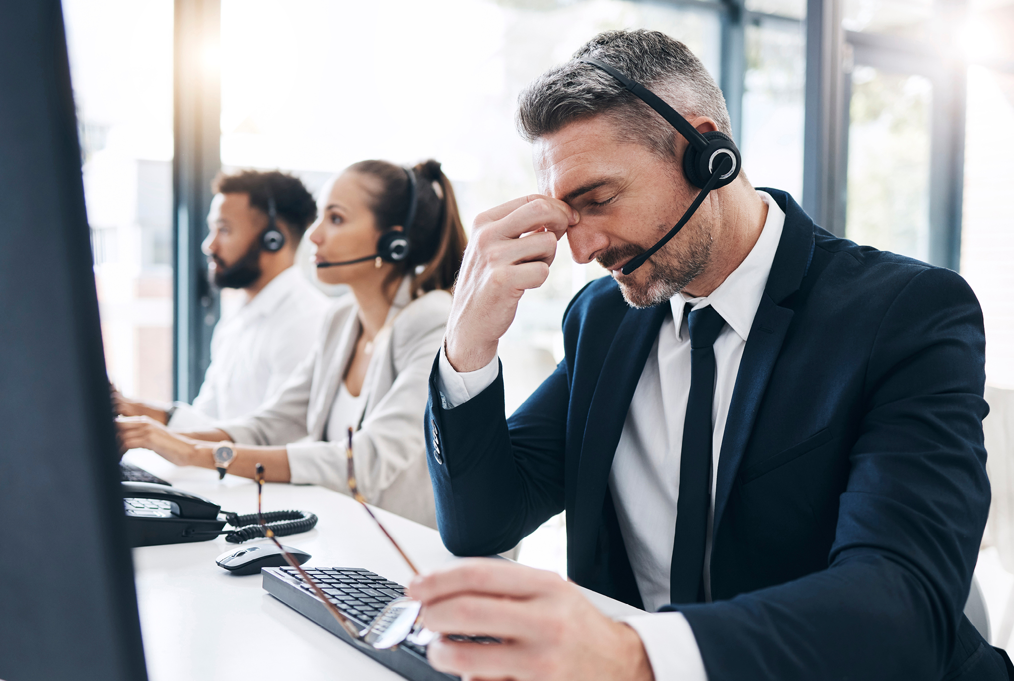 A group of three people sitting at a desk wearing headsets, with one man touching his face