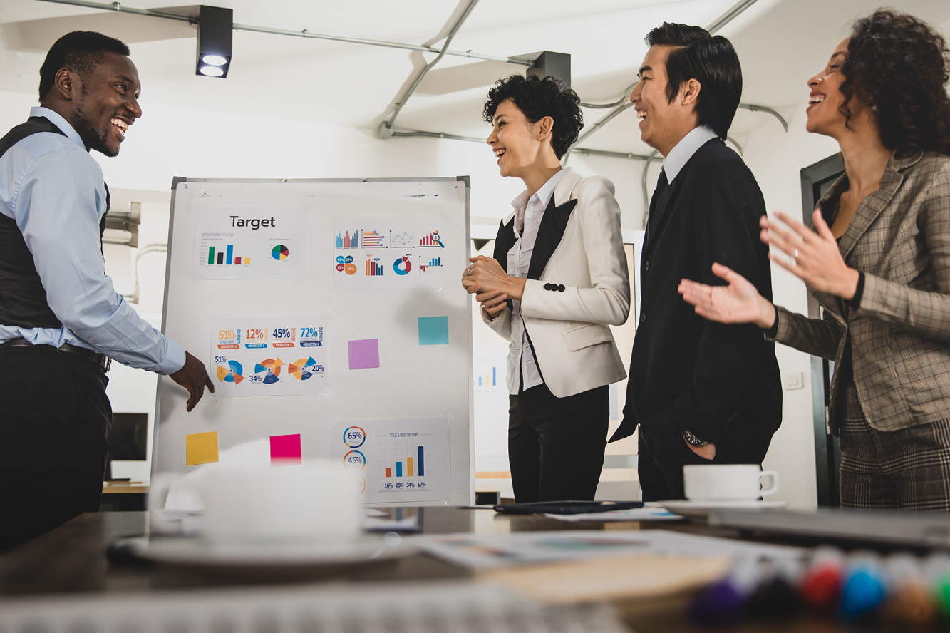 A group of four people standing next to a whiteboard with charts