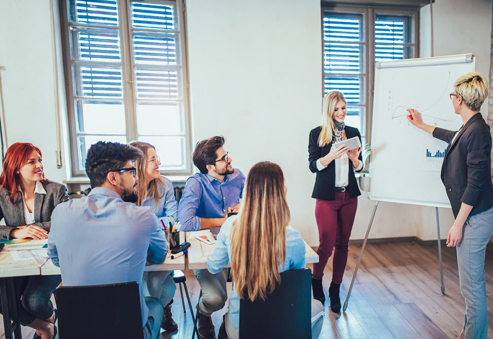 A group of people sitting at a table watching two people give a presentation