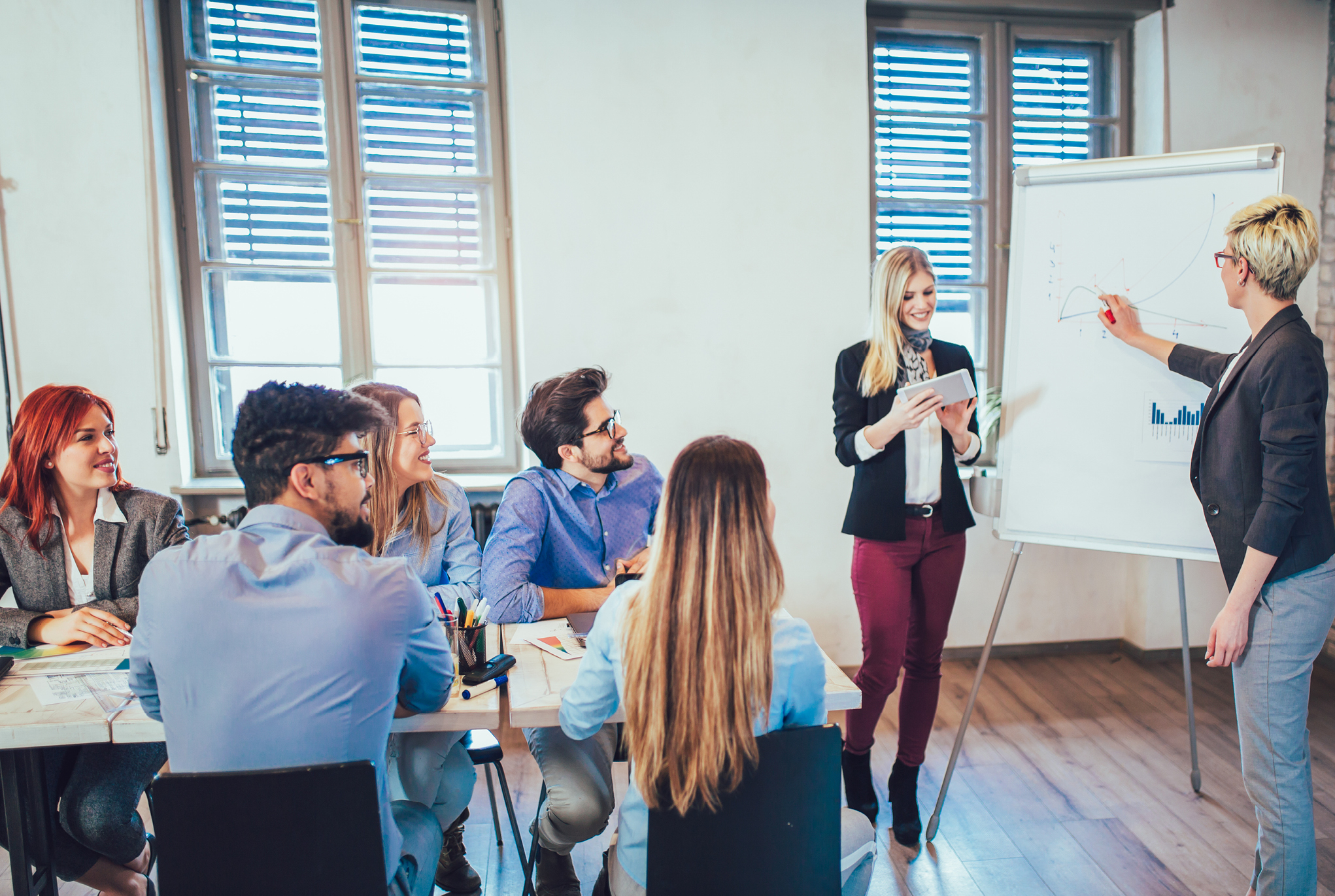 A group of people sitting at a table watching two people give a presentation