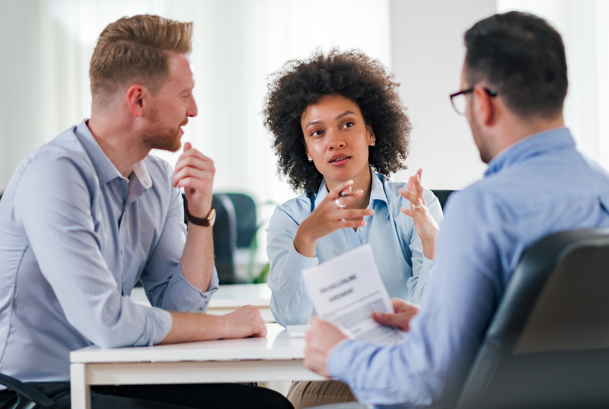 A group of three people in blue button down shirts sitting and talking to each other