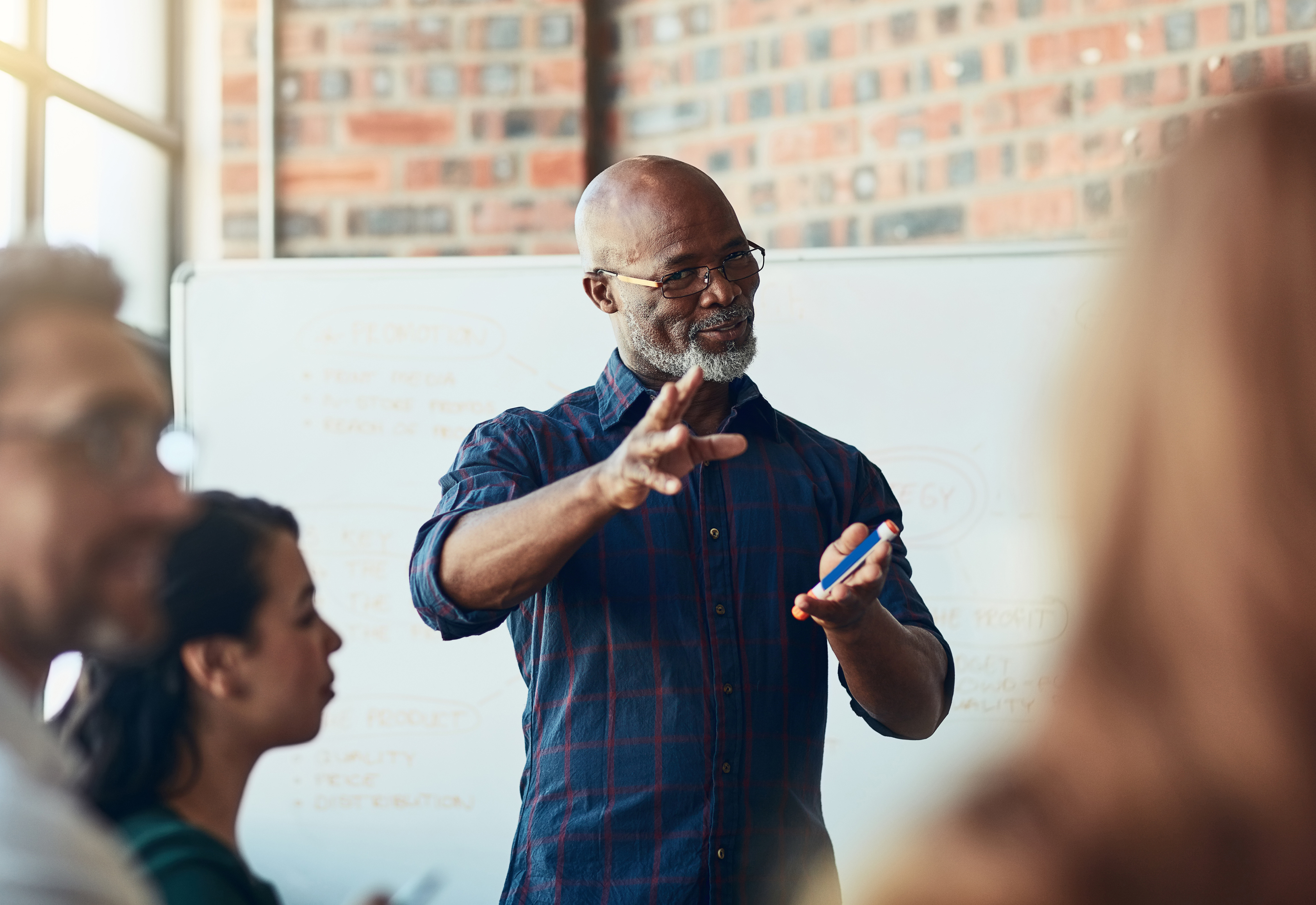 A man with a beard and glasses standing in front of a whiteboard talking to a group of people