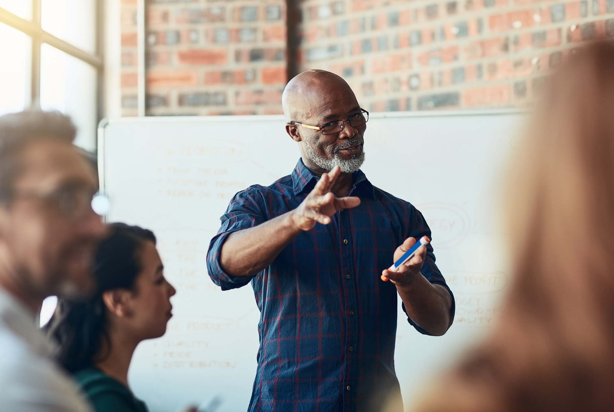 A man with a beard and glasses standing in front of a whiteboard talking to a group of people