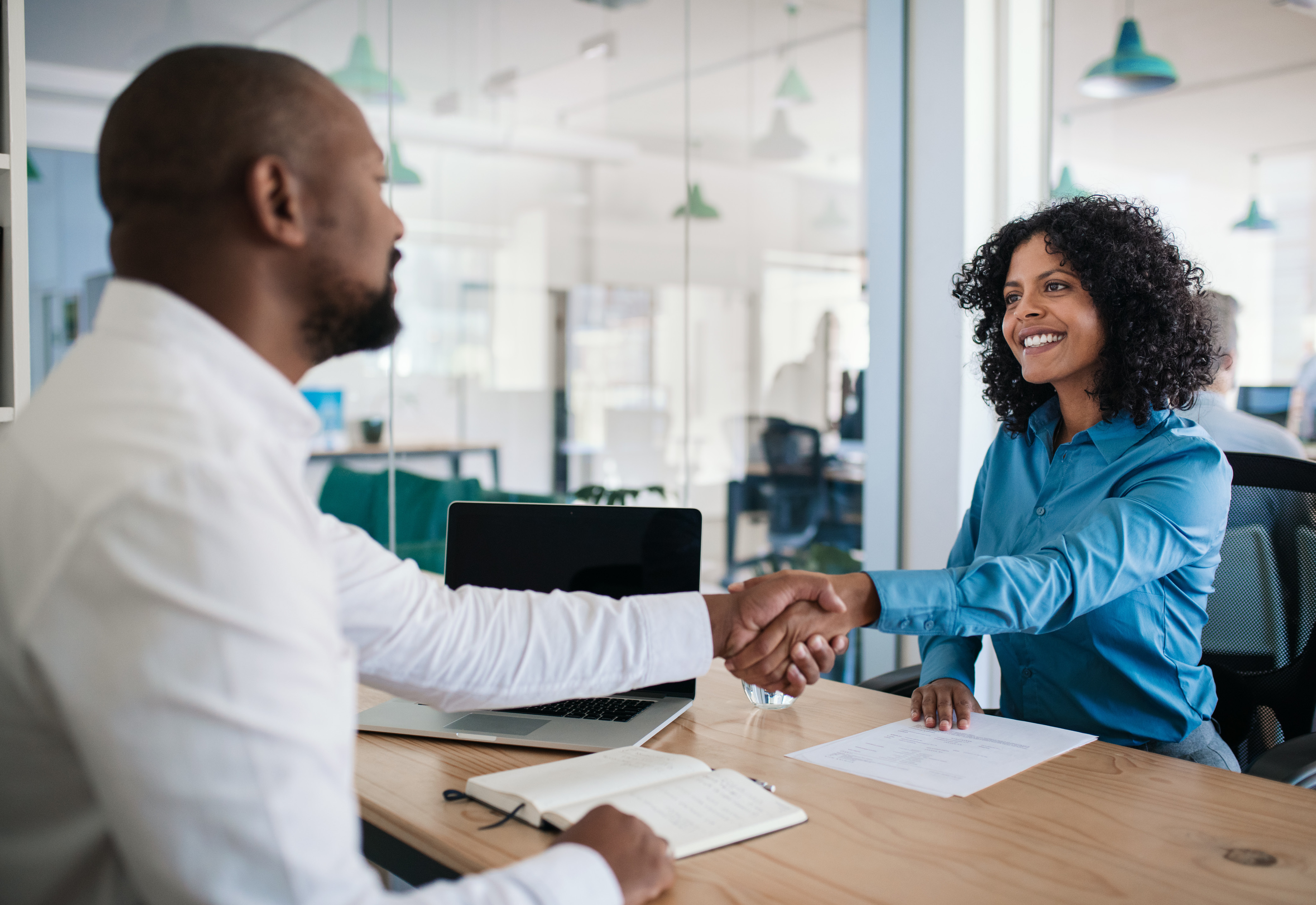 A man and woman sitting at a desk shaking hands