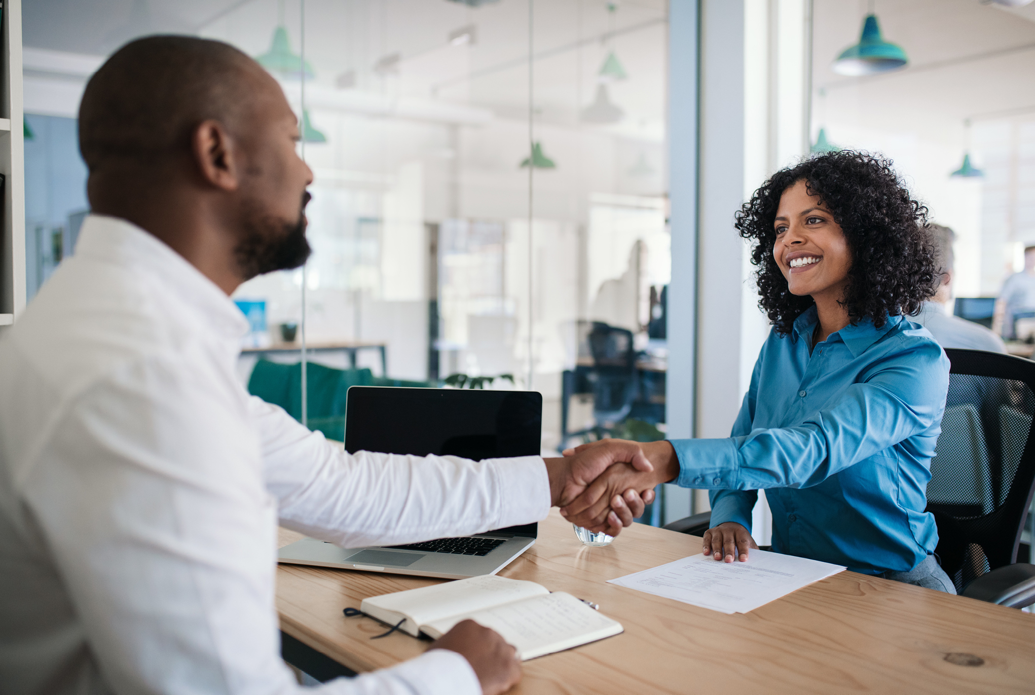 A man and woman sitting at a desk shaking hands