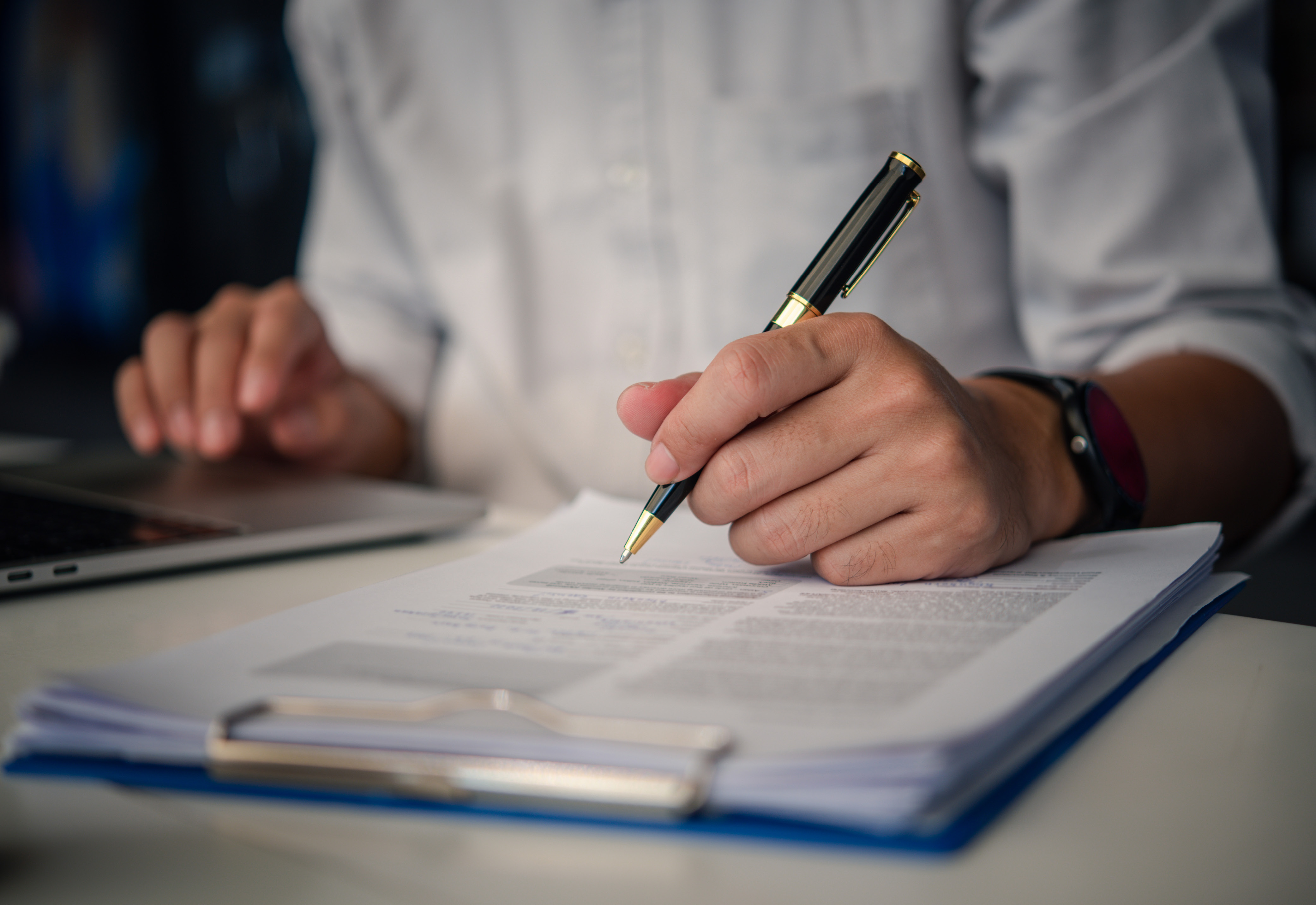 A person holding a pen above a piece of paper on a clipboard