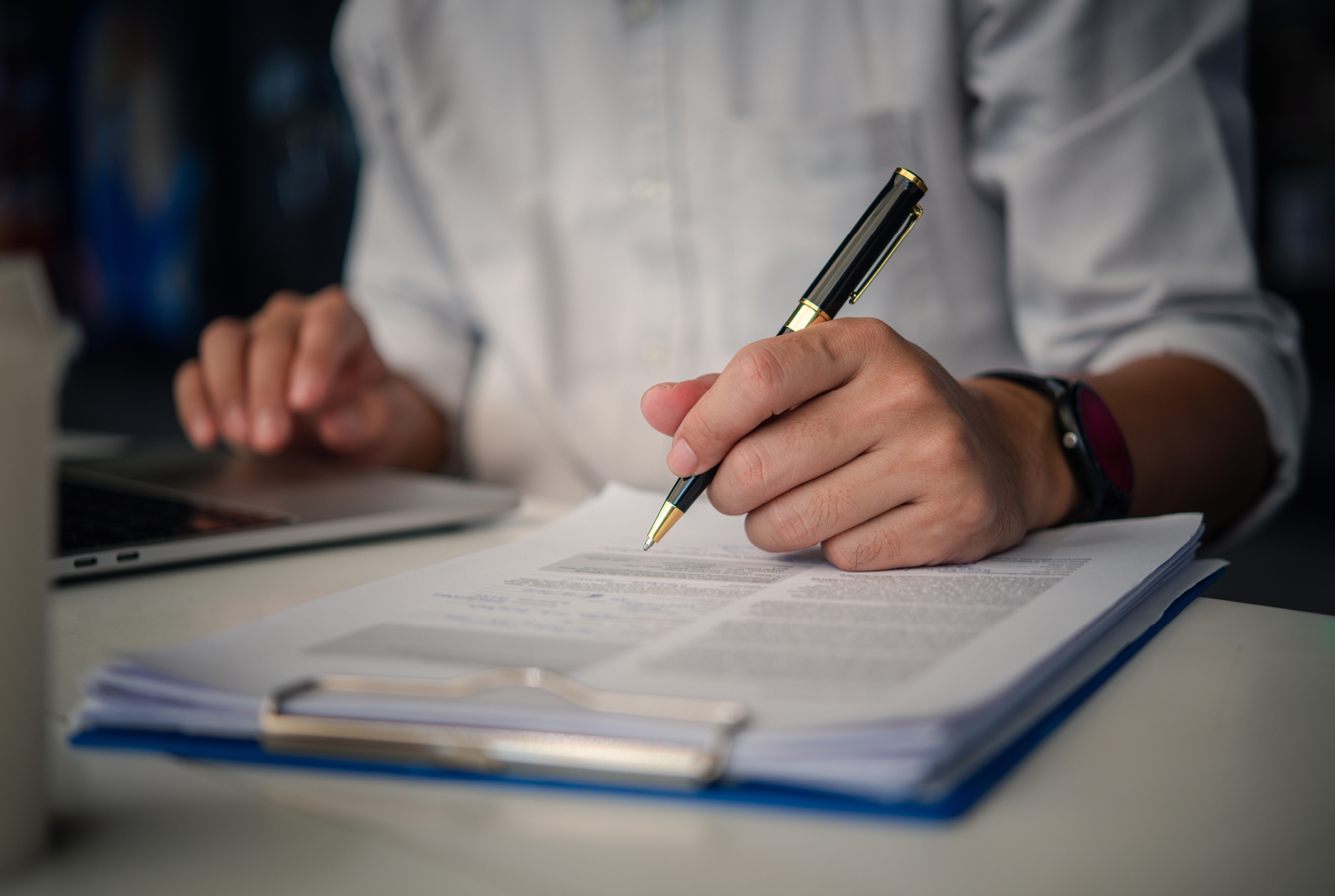 A person holding a pen above a piece of paper on a clipboard