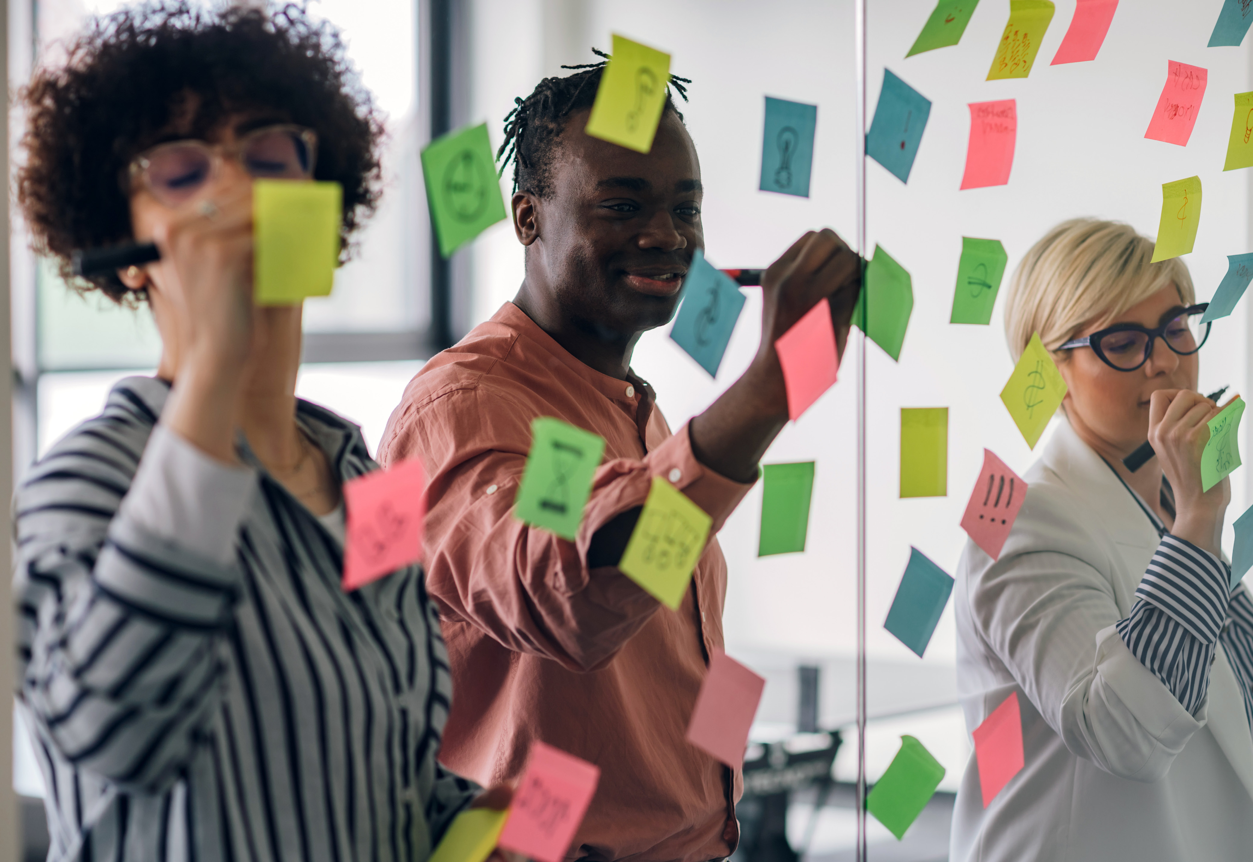 A group of three people writing on sticky notes together