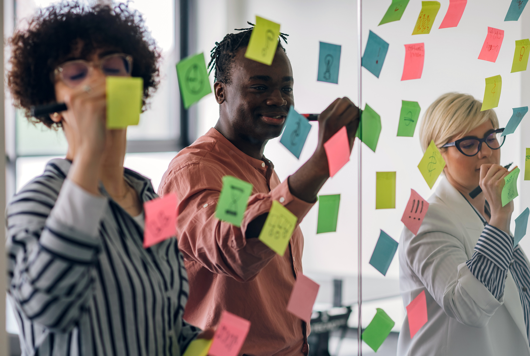 A group of three people writing on sticky notes together