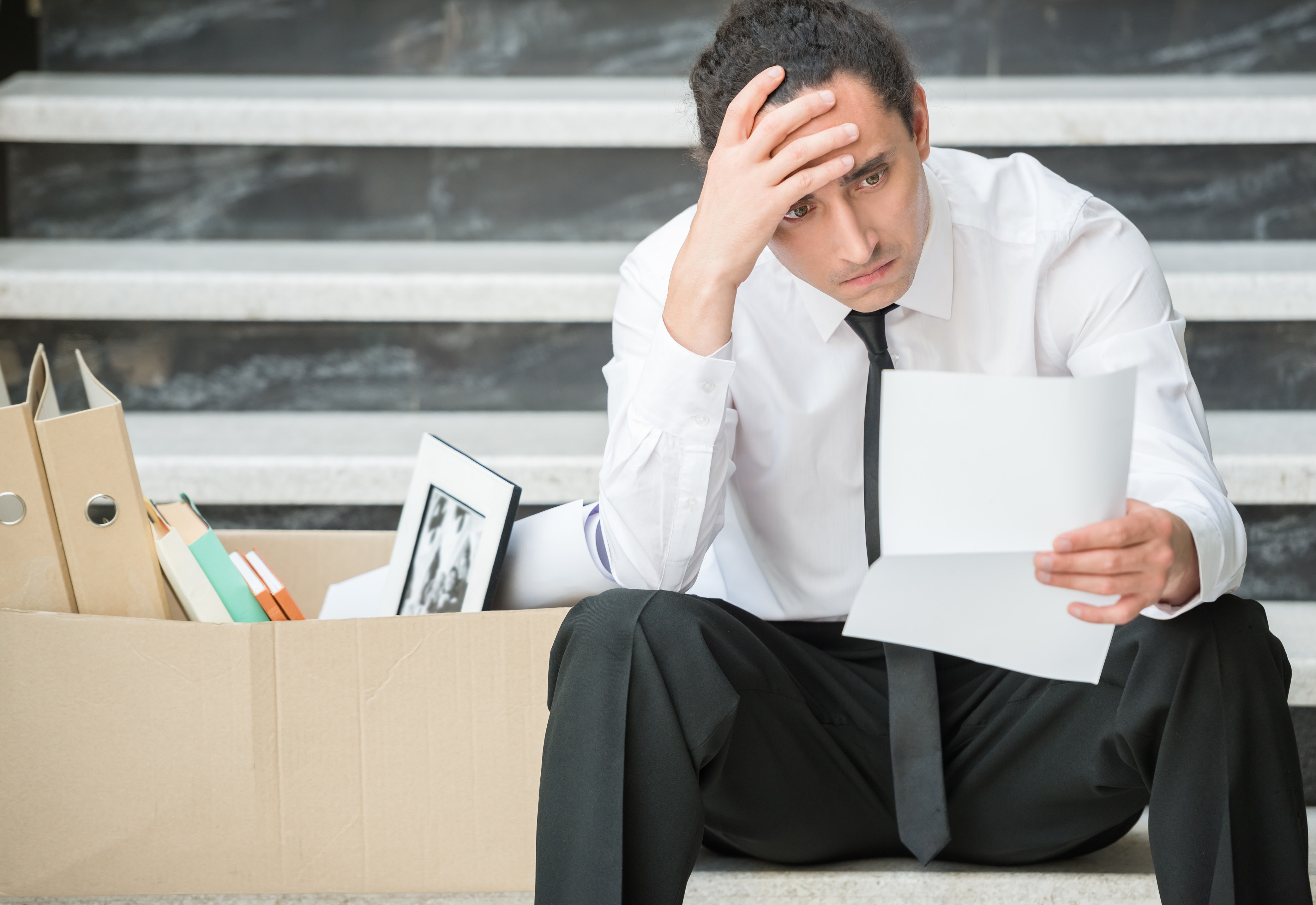 A man in business attire sitting with his hand on his forehead 