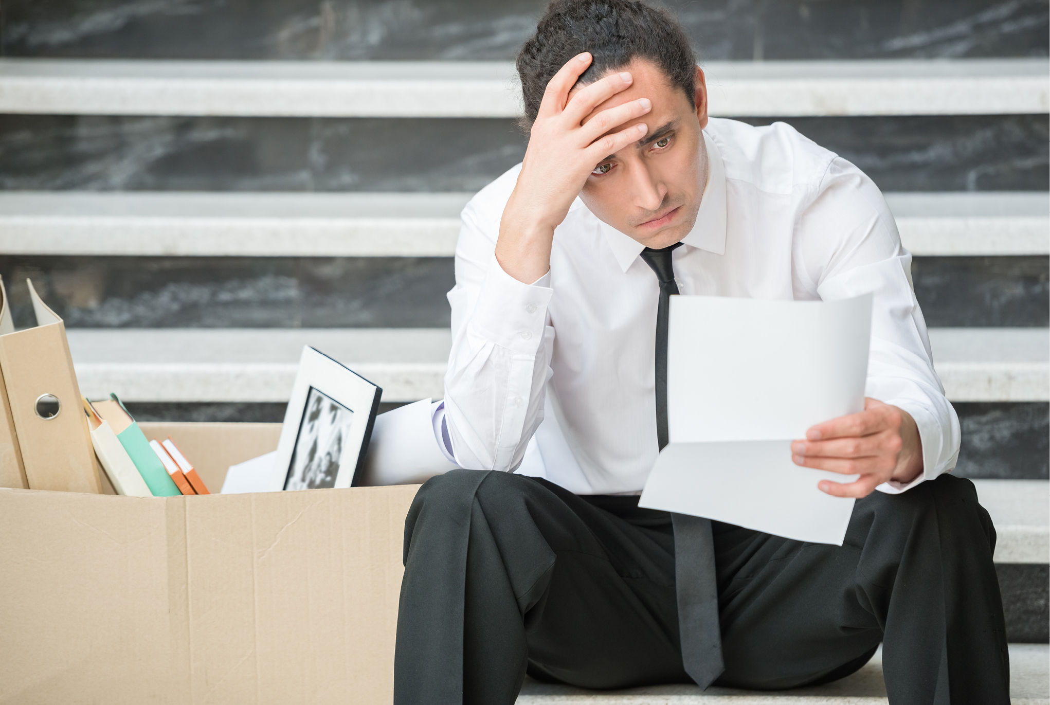 A man in business attire sitting with his hand on his forehead