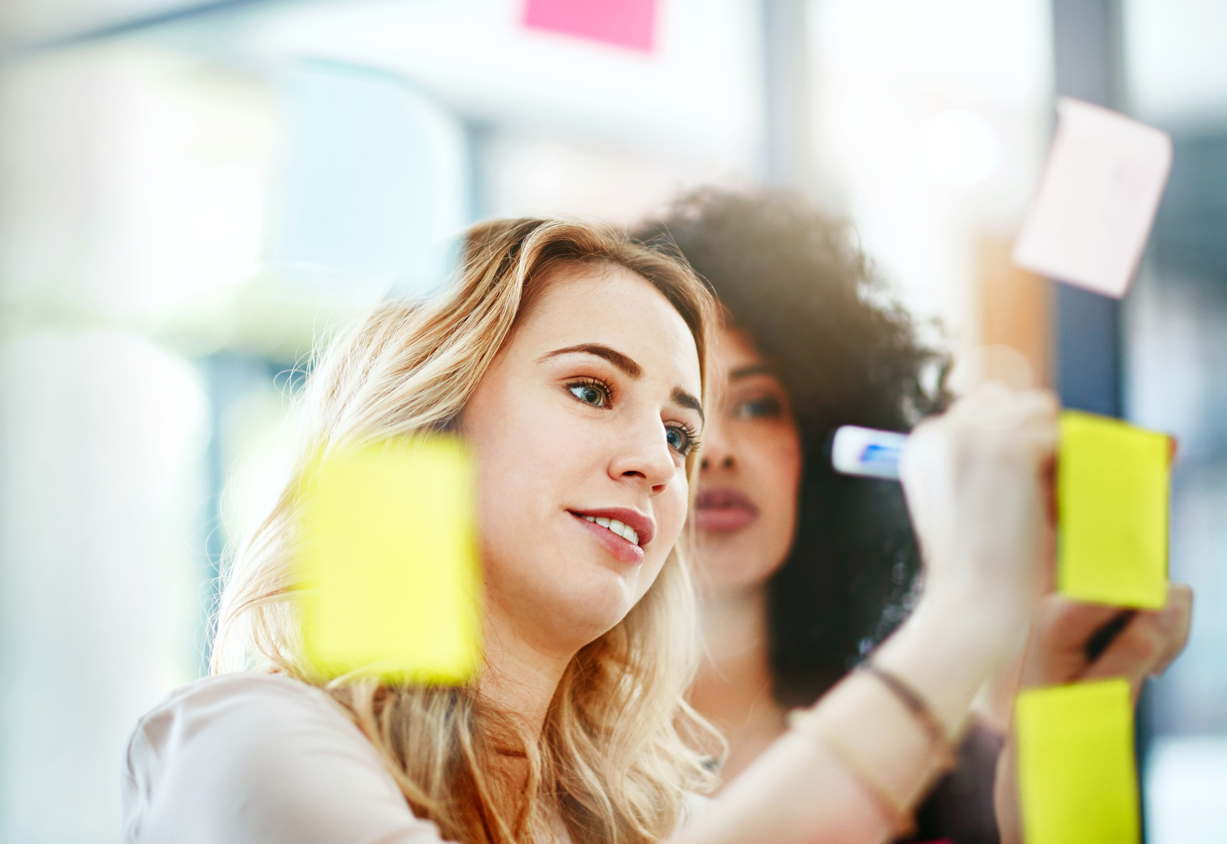 Two women writing on sticky notes on a wall
