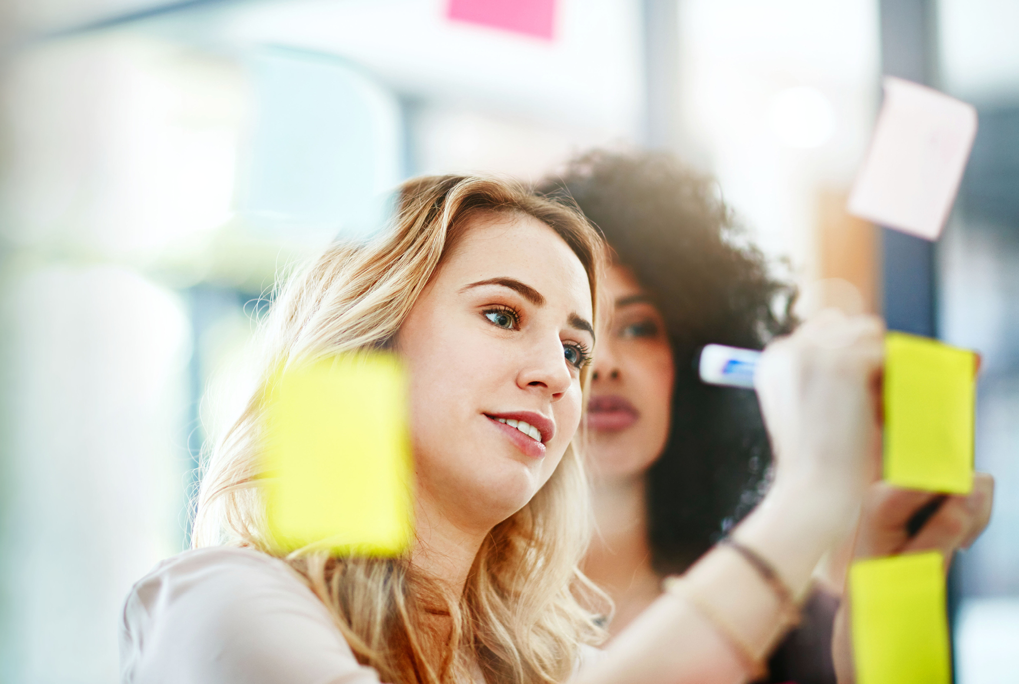 Two women writing on sticky notes on a wall