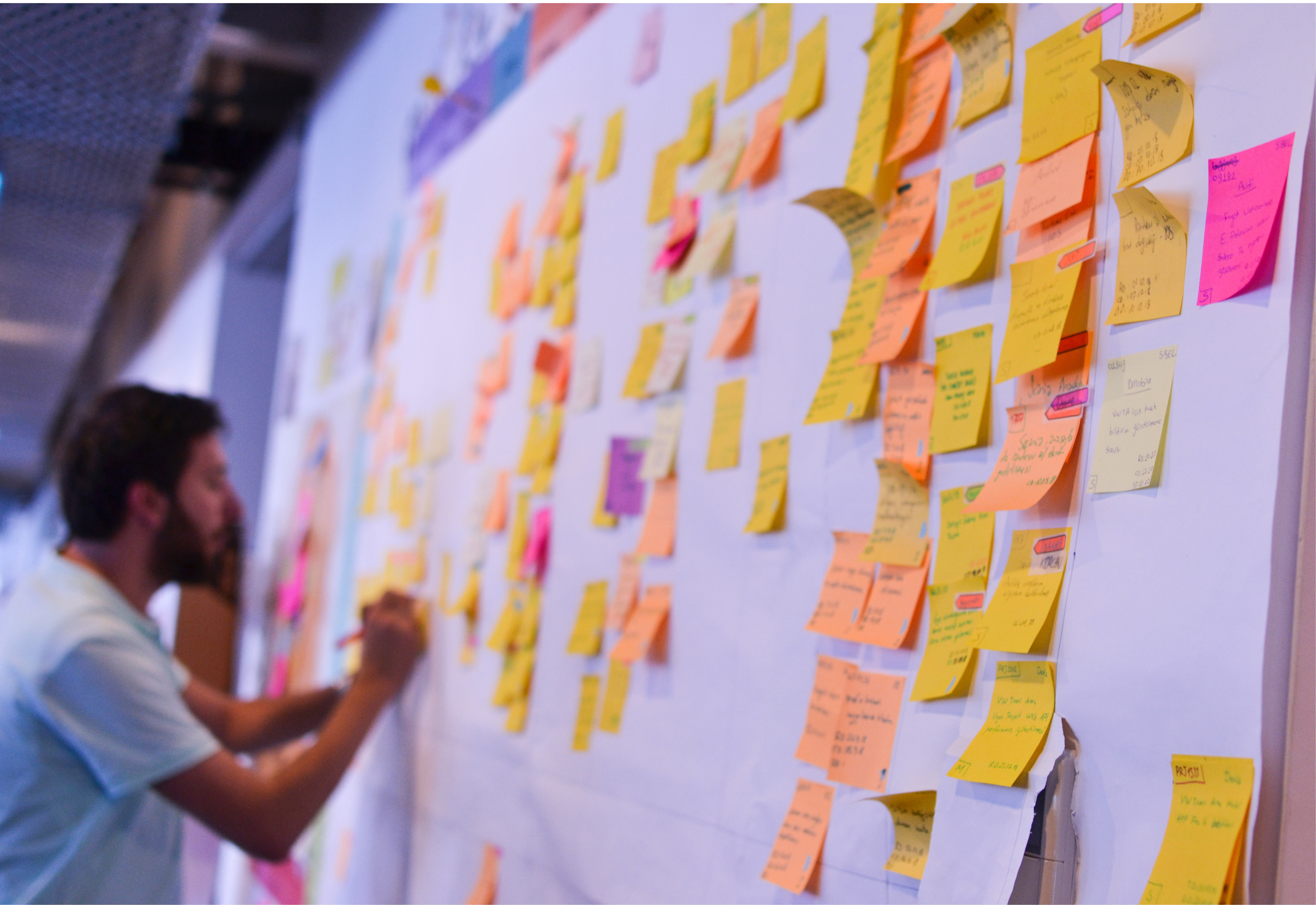A man writing on a wall filled with sticky notes