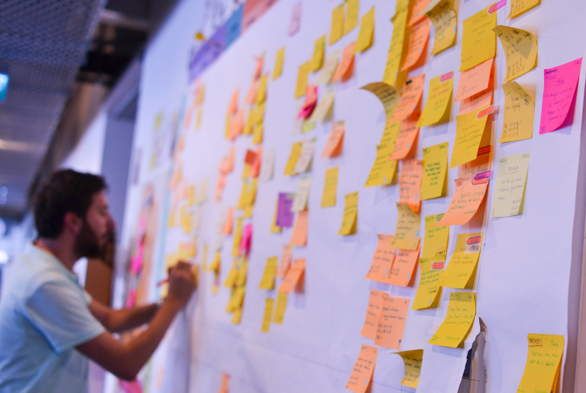 A man writing on a wall filled with sticky notes