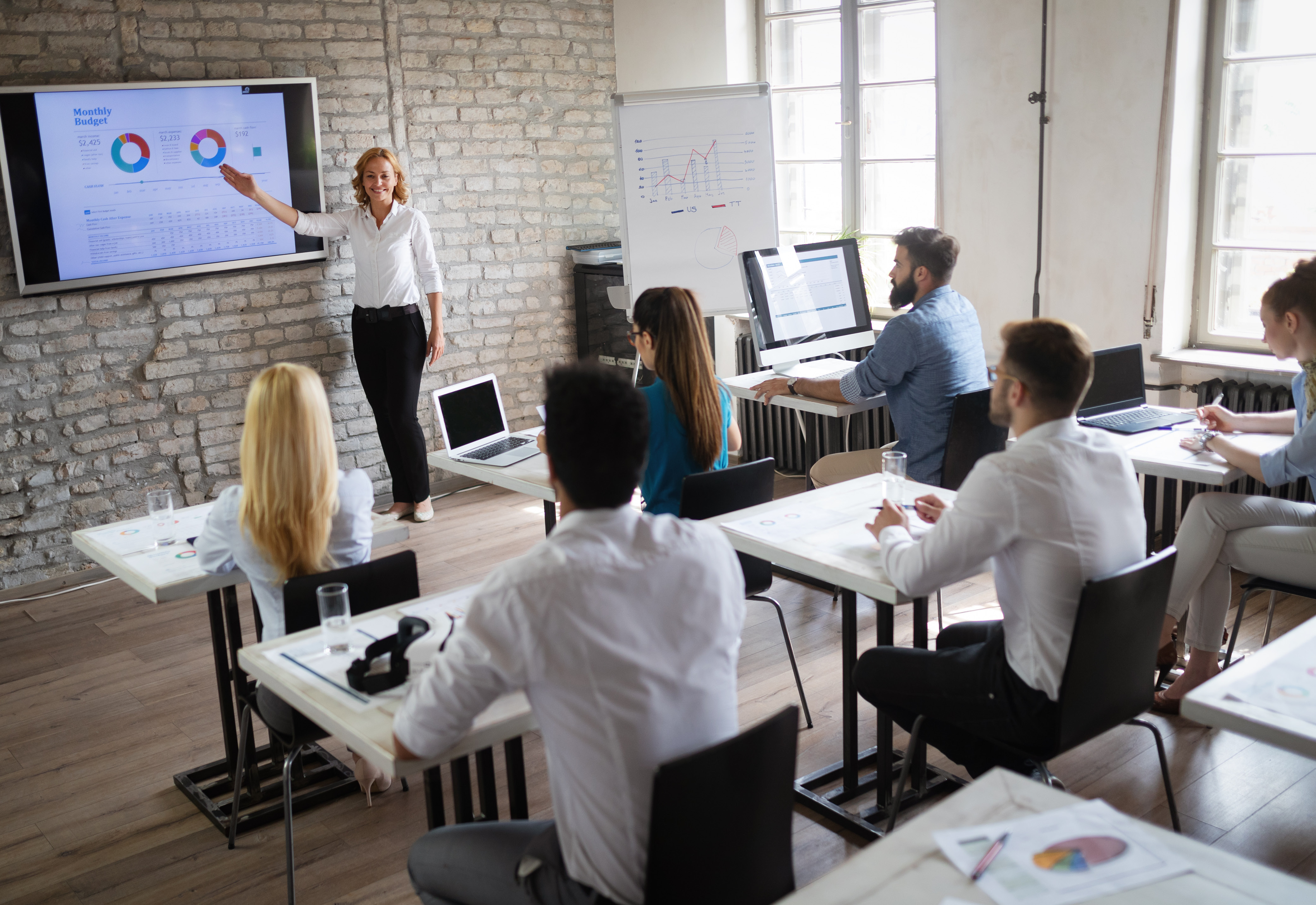 A woman standing at the front of a room presenting a monthly budget to a group of people