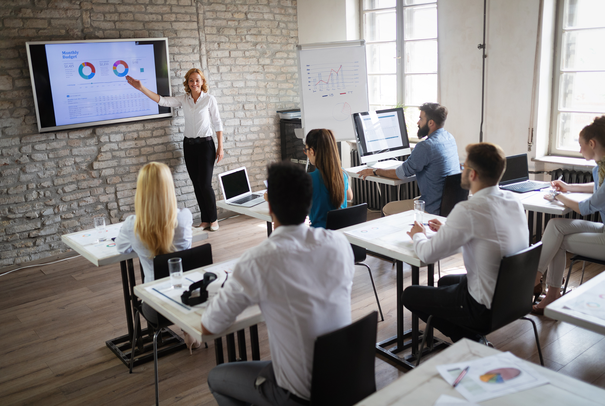A woman standing at the front of a room presenting a monthly budget to a group of people
