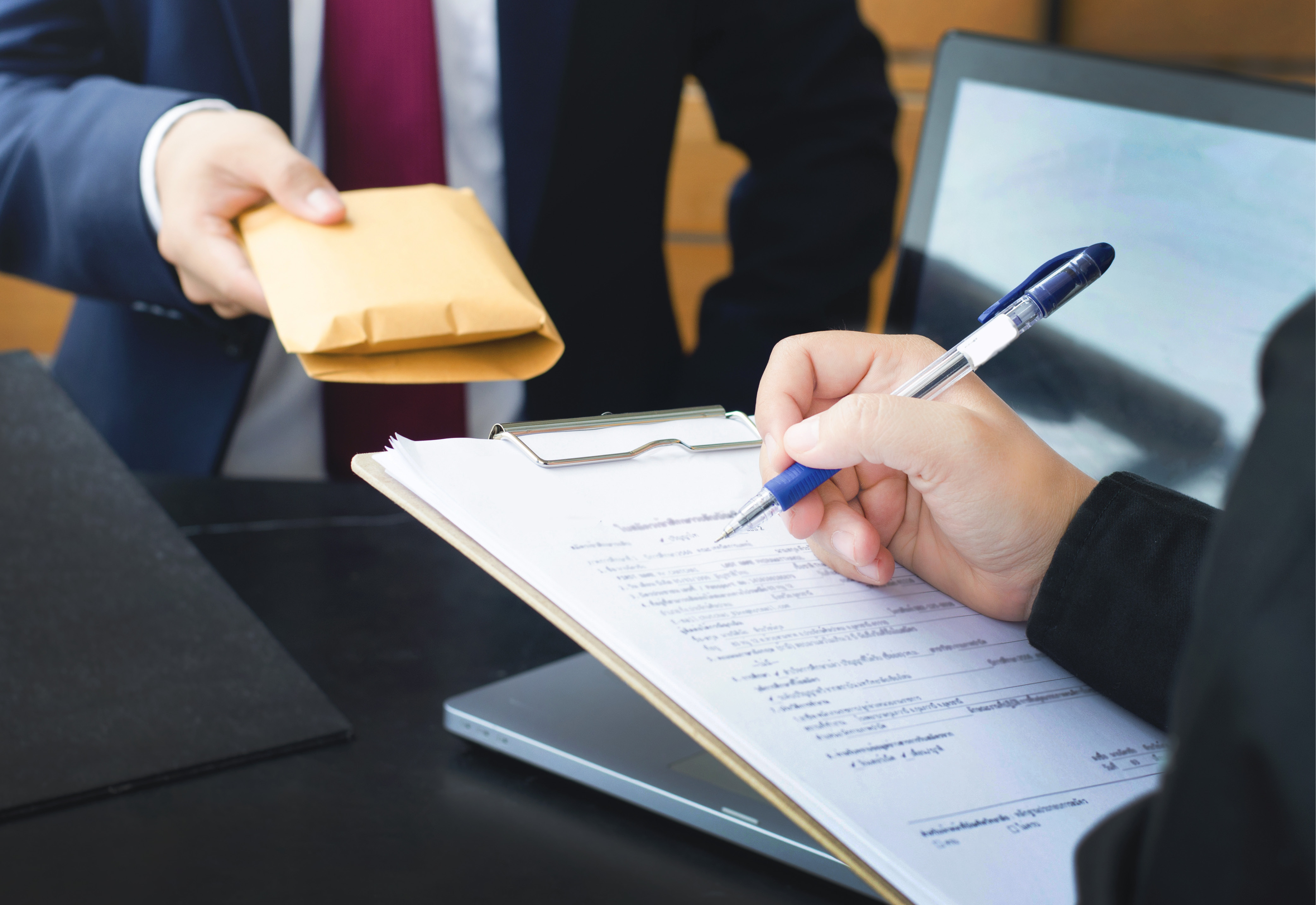 One person writing on a clipboard as another person is handing them an envelope