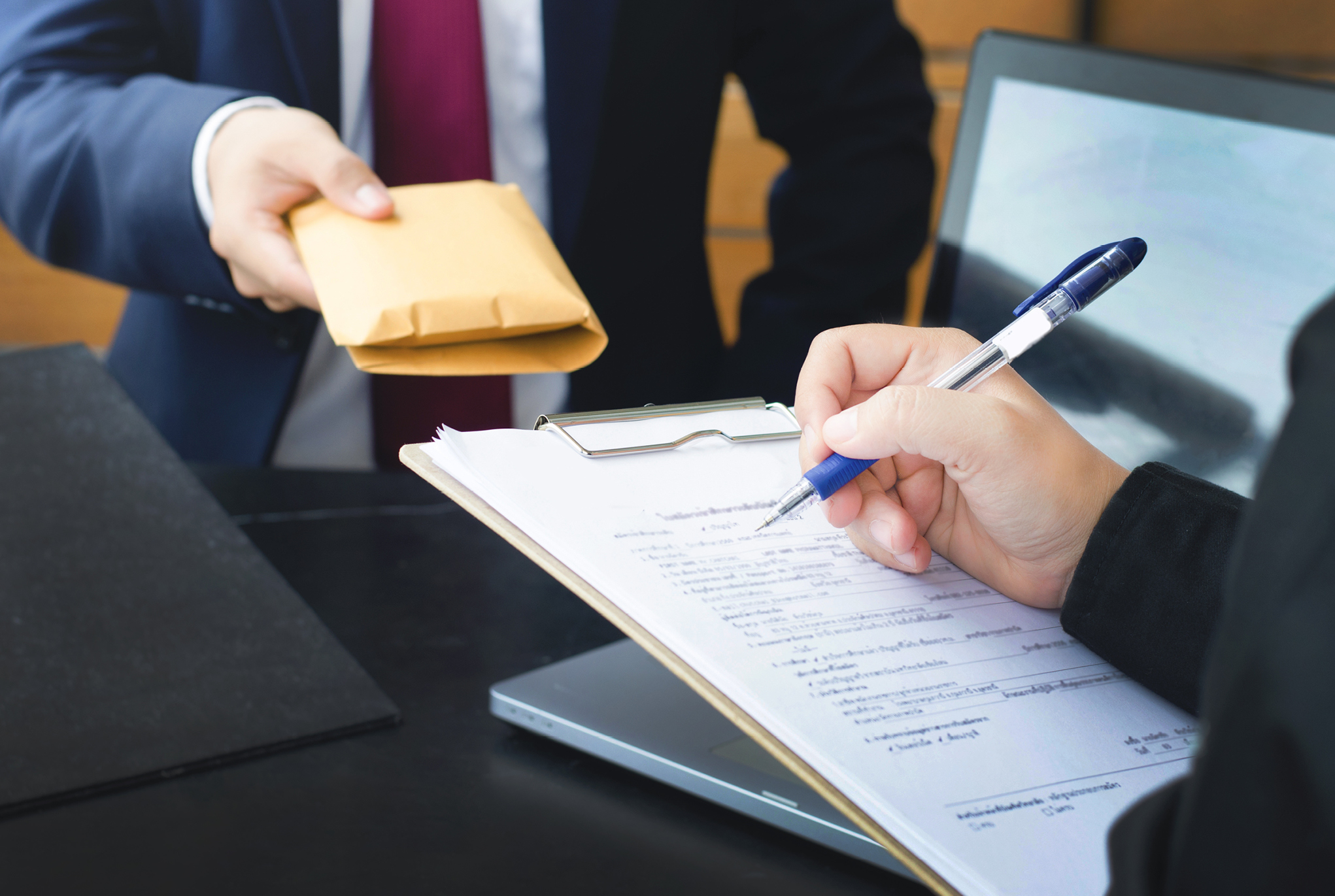 One person writing on a clipboard as another person is handing them an envelope