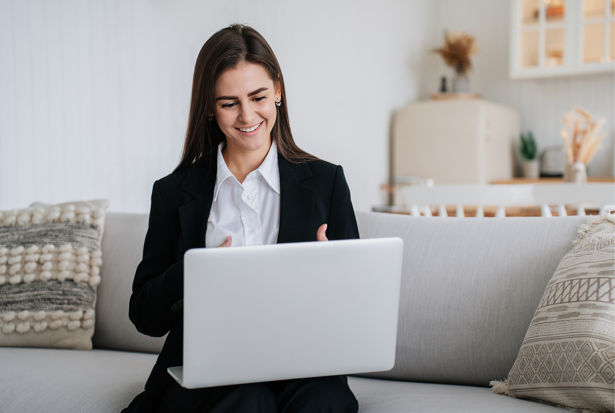 A woman sitting on a sofa having a virtual meeting on her laptop