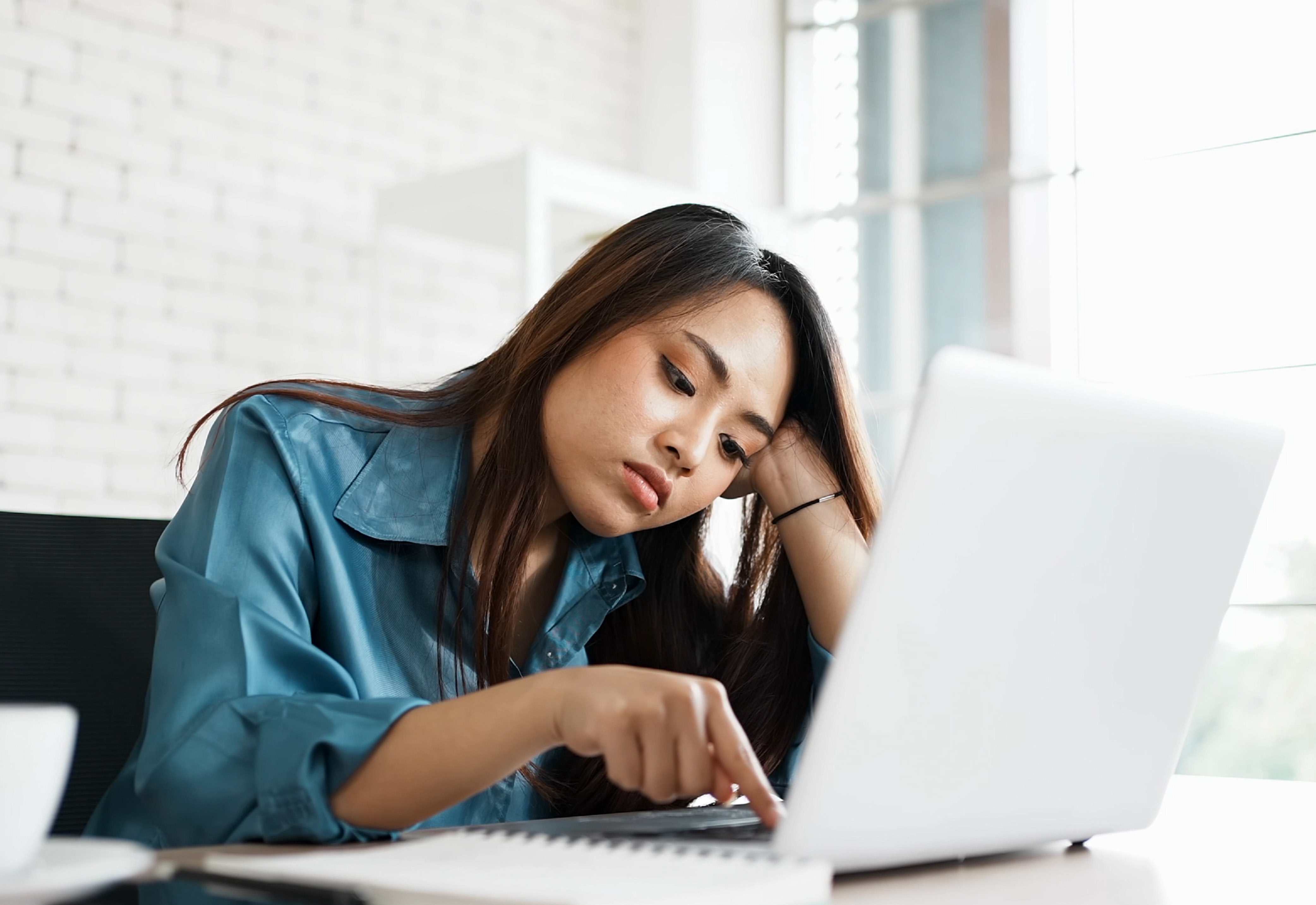 A woman who looks bored typing on her laptop