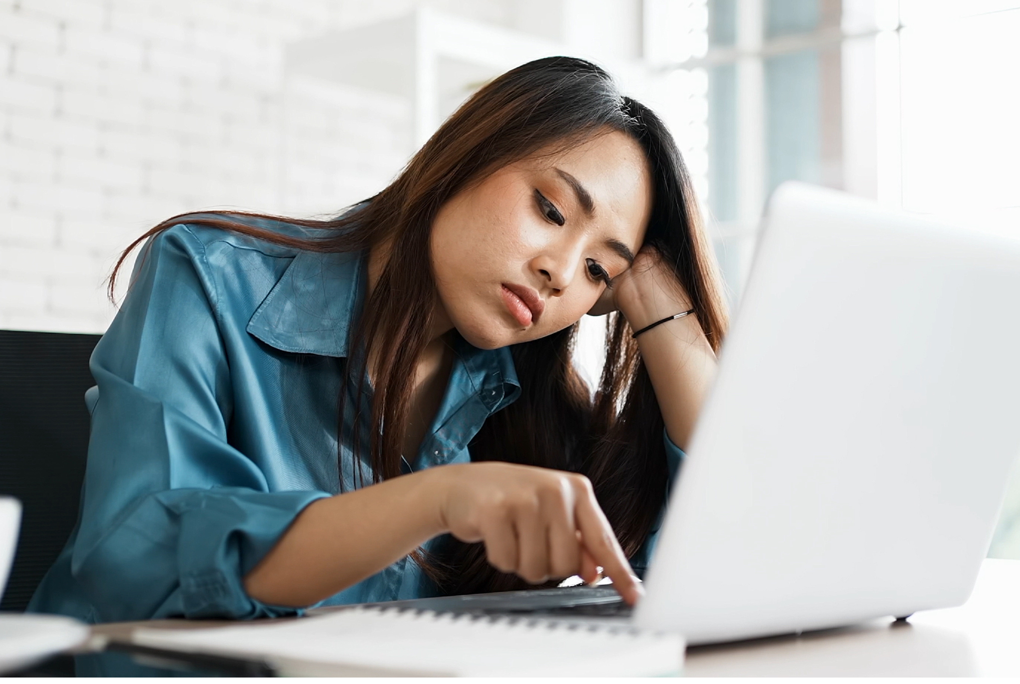 A woman who looks bored typing on her laptop