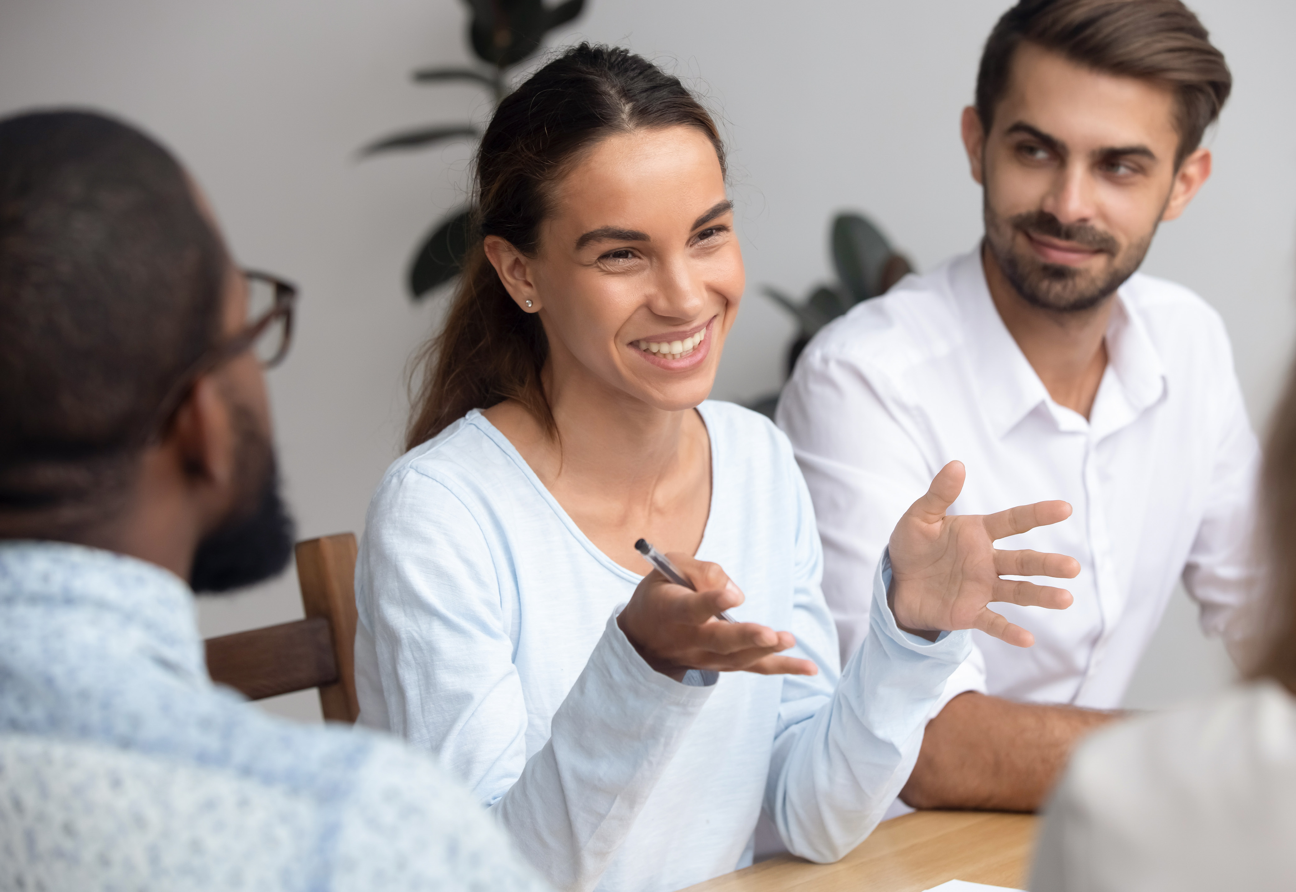 A group of people sitting at a table with a woman smiling and talking with her hands