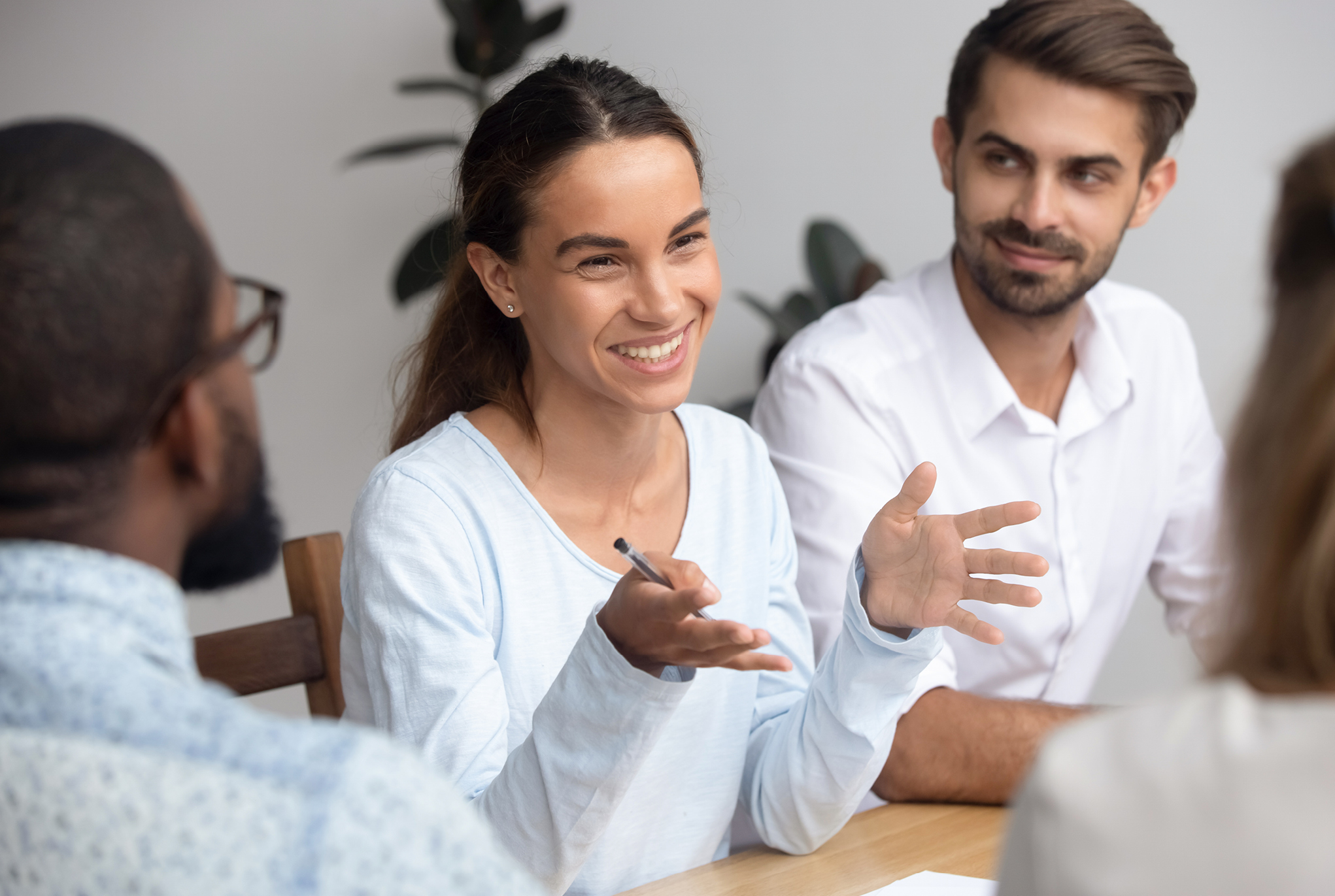 A group of people sitting at a table with a woman smiling and talking with her hands