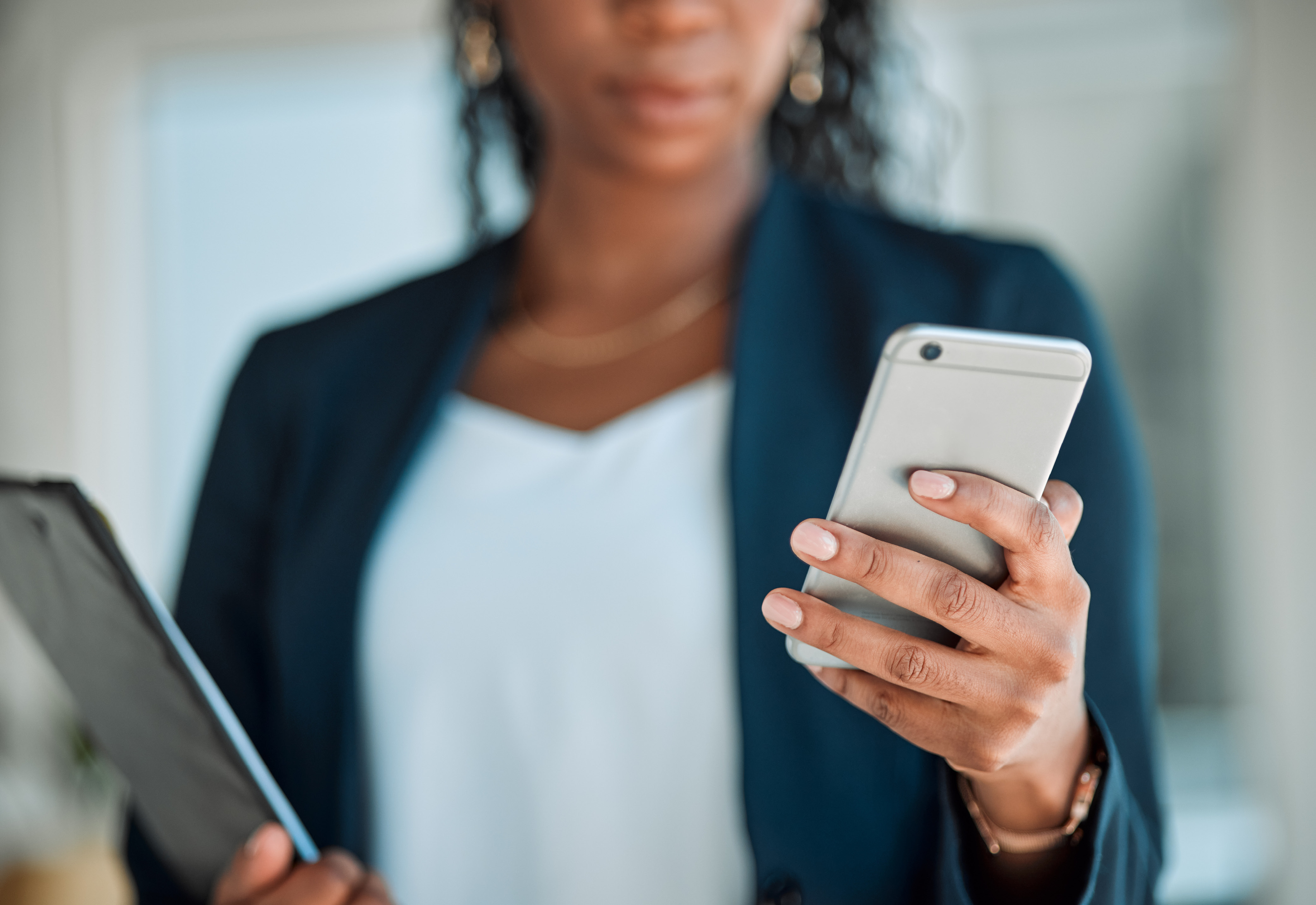 A woman in business attire holding a tablet and a phone